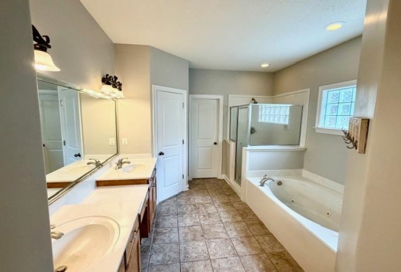 Bathroom featuring a dual vanity with integrated sinks, a separate shower enclosure with glass panels, a built-in tub, and tile flooring