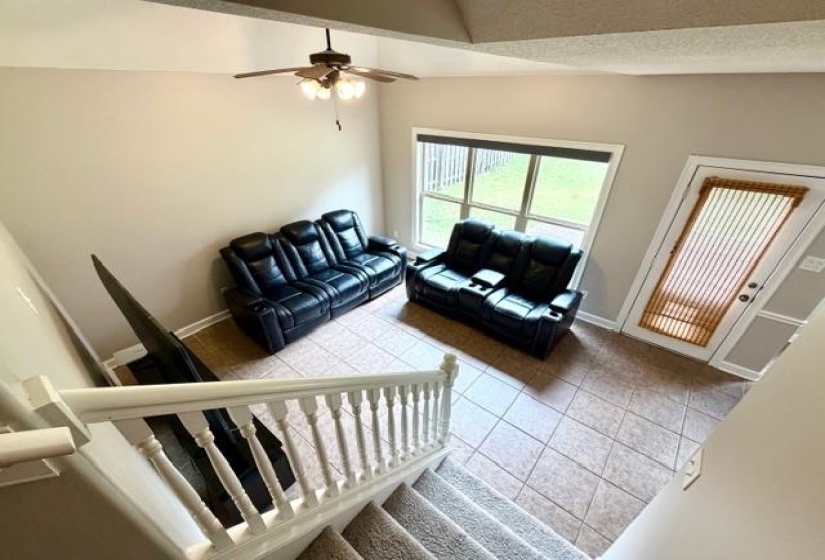 Vaulted ceiling living space featuring tile flooring, a multi-pane window, and a white paneled door with a privacy screen