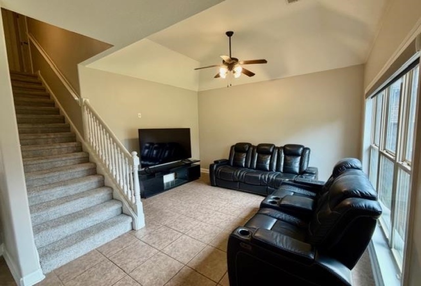 Living area featuring a vaulted ceiling with a ceiling fan, large window, and tile flooring