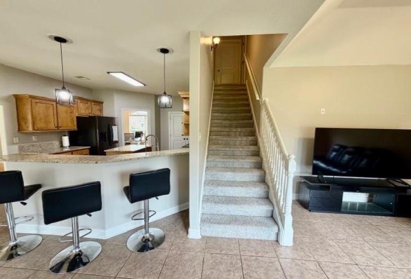 Open concept living space featuring a kitchen with wood cabinetry and a breakfast bar, a staircase with carpeted treads and a white banister, and tile flooring throughout