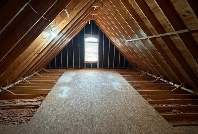 Attic space featuring exposed wood framing, partial subflooring, and an arched window
