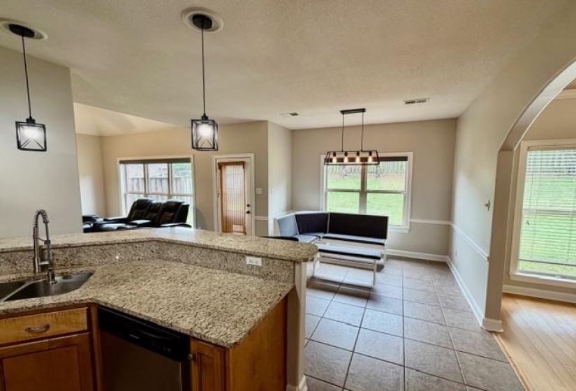 Open-concept kitchen featuring granite countertops, wood-finish cabinetry, and a stainless steel sink with a gooseneck faucet