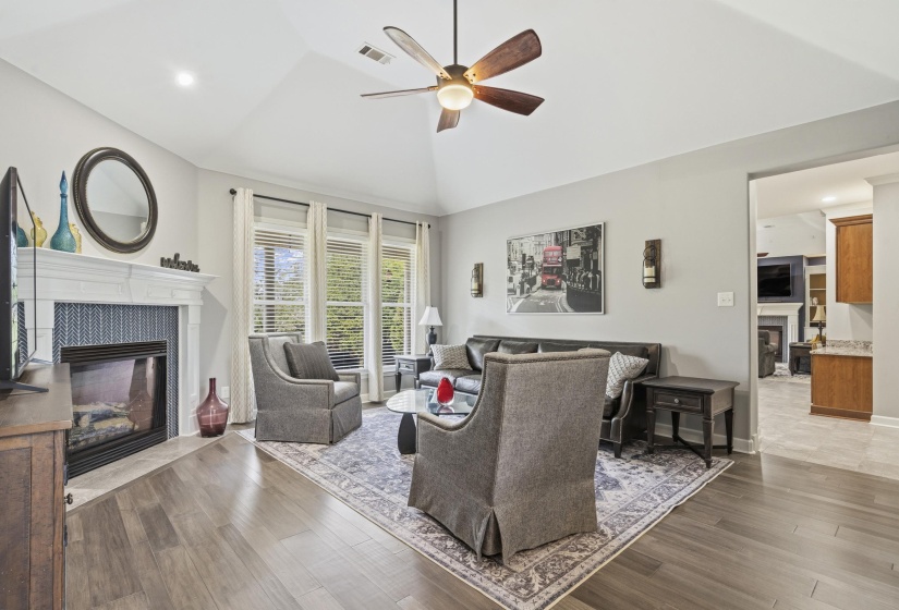 Living area featuring wood-finish flooring, a white mantel fireplace with a patterned tile surround, and an overhead ceiling fan