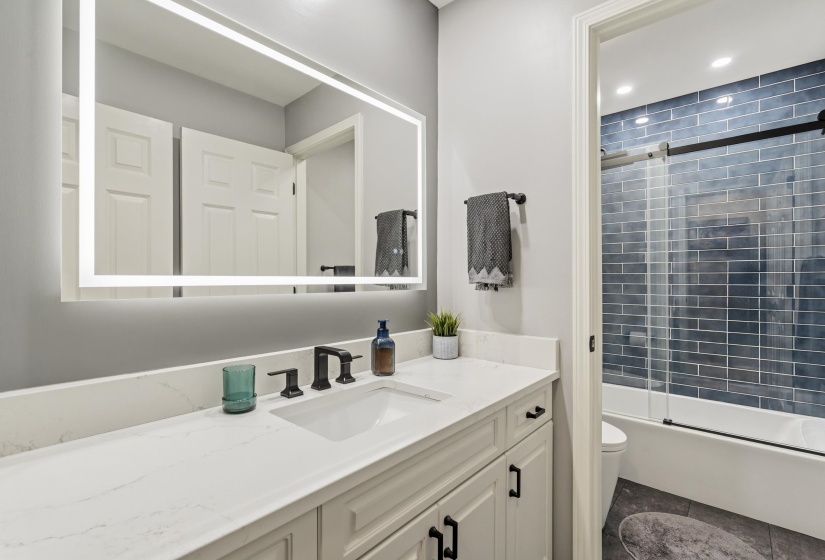 Bathroom featuring an integrated sink vanity with a quartz countertop, an illuminated mirror, and matte black fixtures