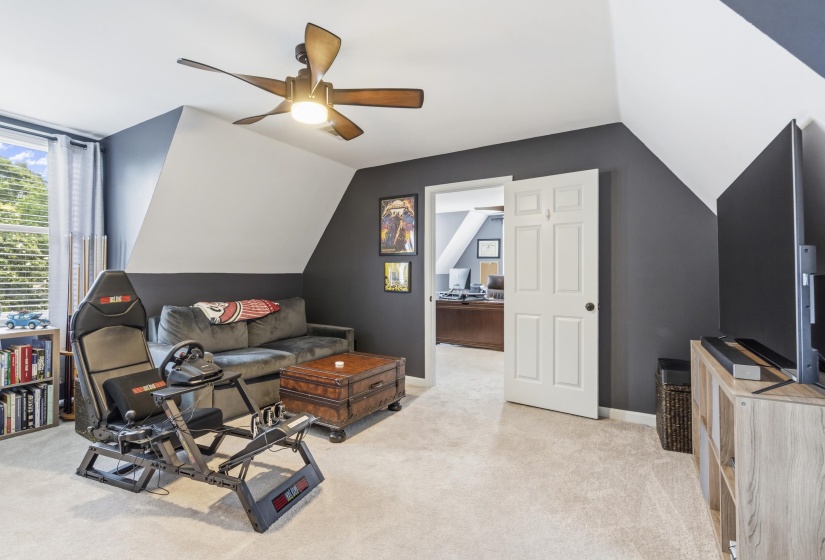Carpeted room with sloped ceilings, featuring a ceiling fan with integrated lighting