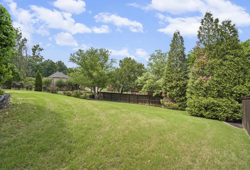 Expansive backyard featuring a lush lawn, mature trees and shrubs, and a privacy fence