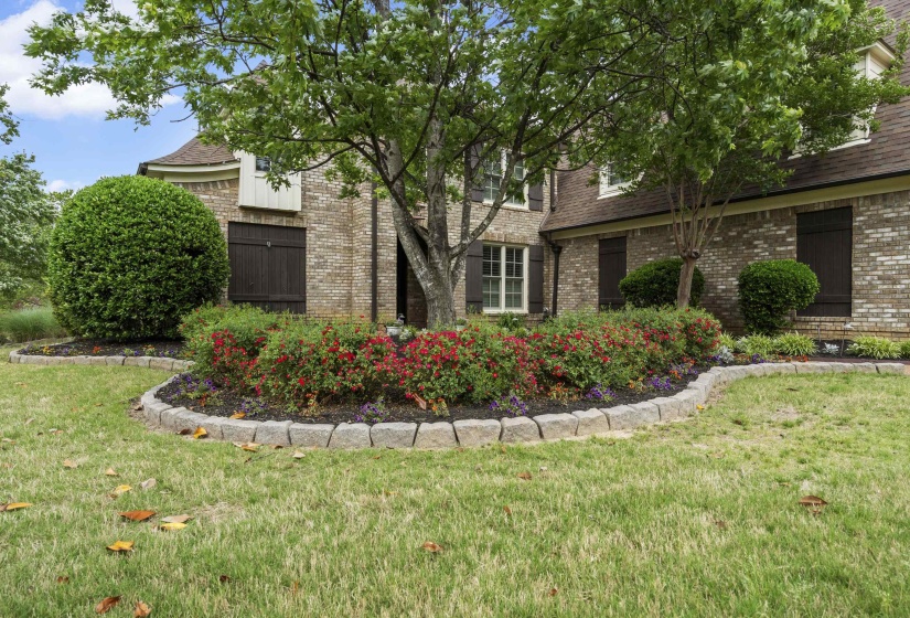 Brick exterior featuring dark shutters and a curved stone-edged garden bed with red and purple plantings