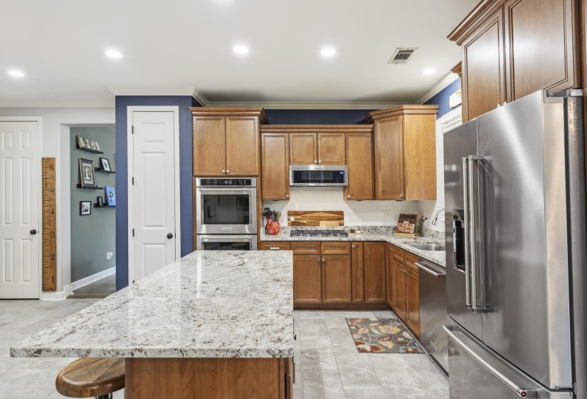 Kitchen featuring a large central island with a light-toned countertop, wood-finish cabinetry, stainless steel appliances, and recessed lighting