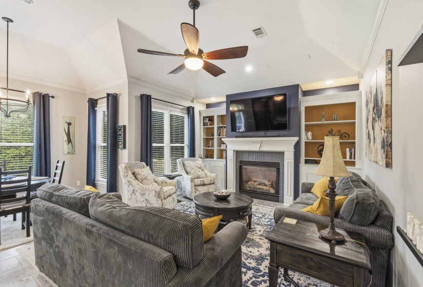 Living area featuring a fireplace with a detailed mantel, built-in shelving, high vaulted ceilings, and a ceiling fan