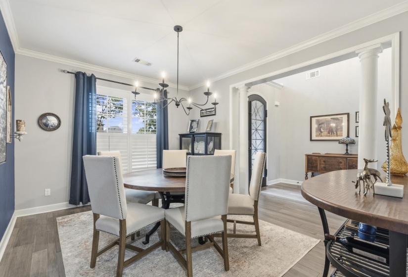 Formal dining area featuring wood-finish flooring, a contemporary chandelier, crown molding, and decorative wall columns