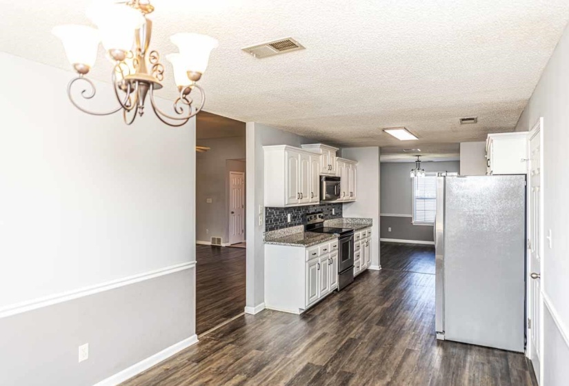 Kitchen featuring hanging light fixtures, a chandelier, stainless steel appliances, a textured ceiling, and dark stone countertops