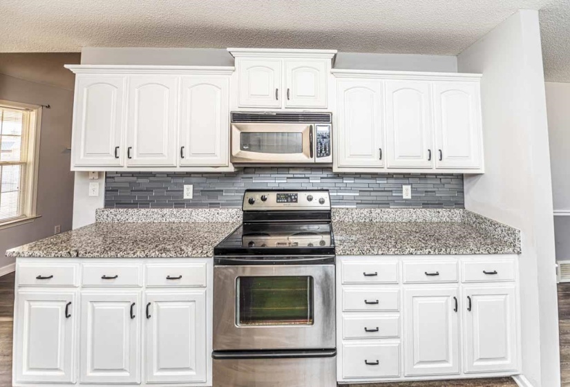 Kitchen with appliances with stainless steel finishes, light stone countertops, a textured ceiling, dark wood-style floors, and white cabinetry