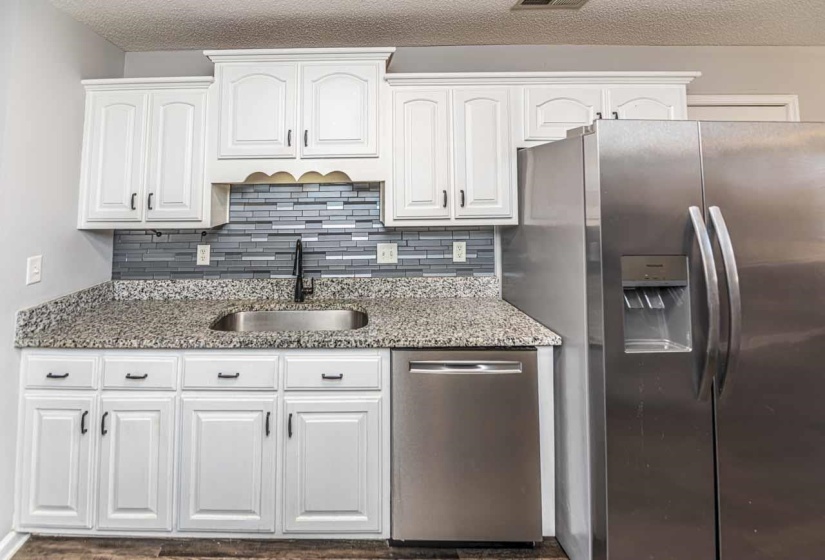 Kitchen with light stone counters, appliances with stainless steel finishes, white cabinetry, a textured ceiling, and tasteful backsplash