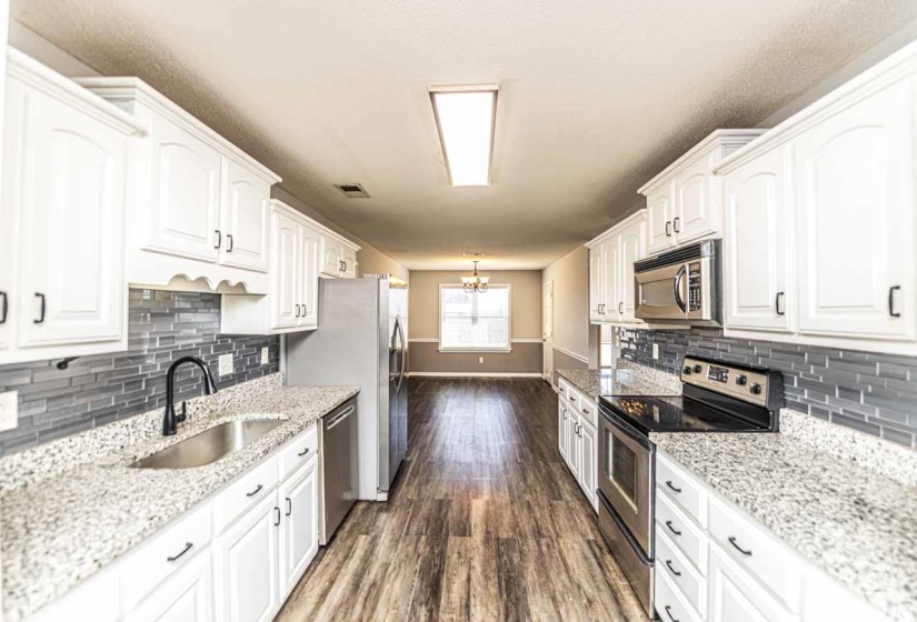 Kitchen with stainless steel appliances, white cabinetry, and light stone countertops