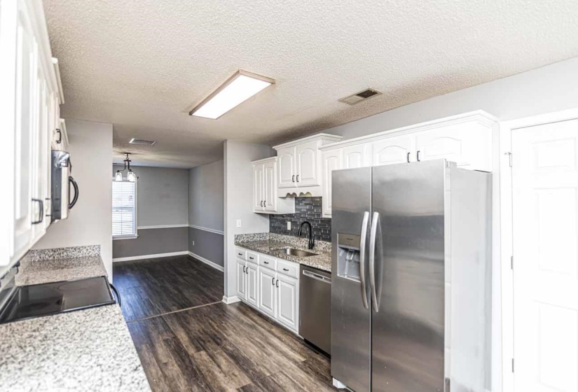 Kitchen featuring white cabinetry, light stone countertops, a textured ceiling, appliances with stainless steel finishes, and dark wood finished floors
