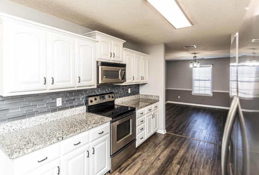 Kitchen featuring stainless steel appliances, white cabinets, light stone countertops, a textured ceiling, and dark wood-style floors