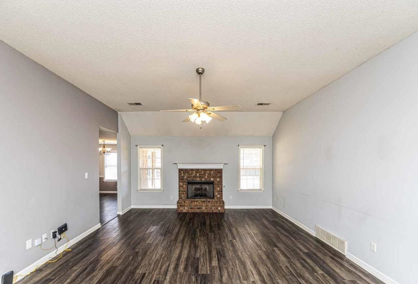 Unfurnished living room with dark wood-type flooring, lofted ceiling, a textured ceiling, ceiling fan, and a brick fireplace