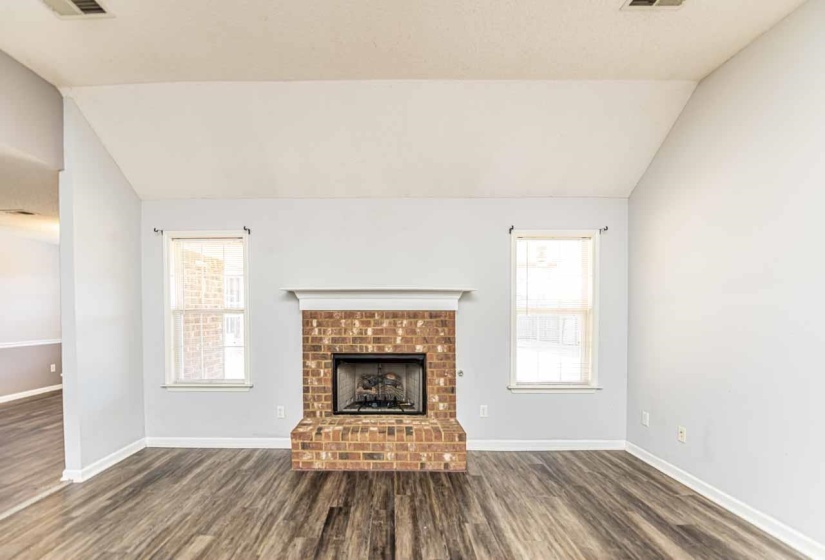 Unfurnished living room with vaulted ceiling, a fireplace, and dark wood-style flooring