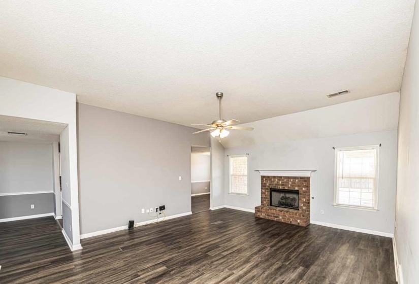 Unfurnished living room with a textured ceiling, dark wood-style flooring, a fireplace, and a ceiling fan