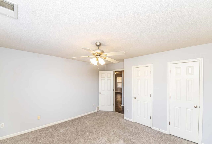 Unfurnished bedroom featuring a textured ceiling, carpet flooring, multiple closets, and ceiling fan