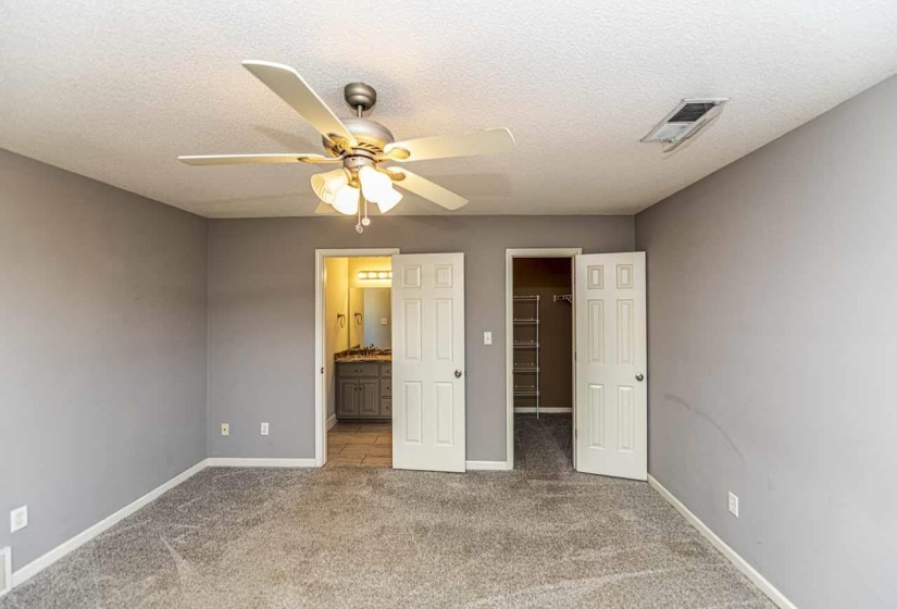 Unfurnished bedroom featuring a walk in closet, carpet floors, a textured ceiling, ensuite bathroom, and ceiling fan
