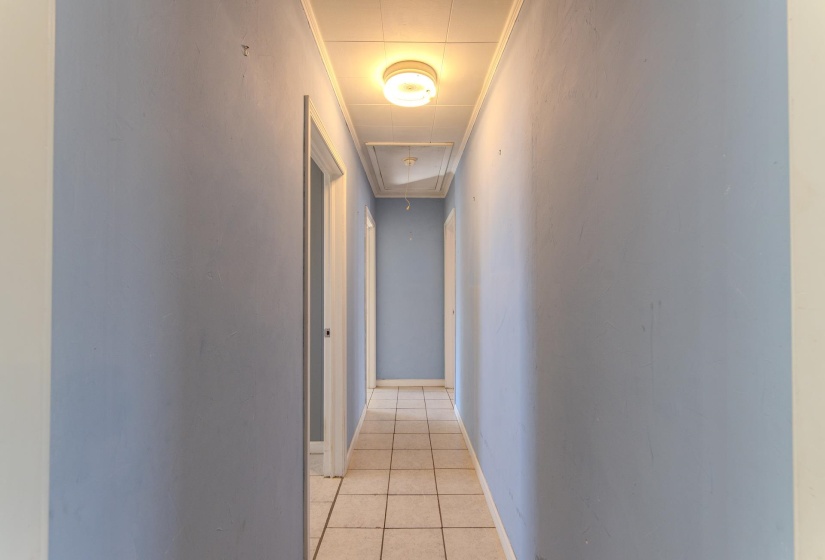 Hall featuring light tile patterned floors, attic access, and crown molding