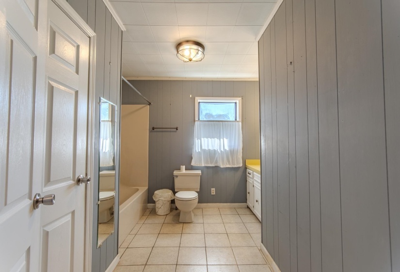 Bathroom featuring wood walls, light tile patterned floors, washtub / shower combination, vanity, and ornamental molding