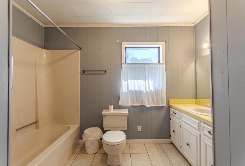 Bathroom with light tile patterned floors, vanity, crown molding, wooden walls, and shower / bath combination