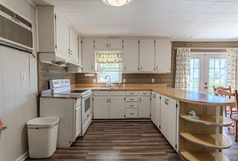 Kitchen featuring light countertops, a peninsula, electric stove, wood walls, and healthy amount of natural light