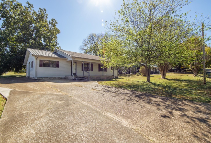 Ranch-style home featuring concrete driveway, a metal roof, a front lawn, and covered porch