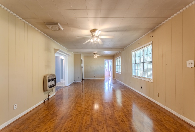 Unfurnished living room with wooden walls, ornamental molding, wood finished floors, heating unit, and ceiling fan
