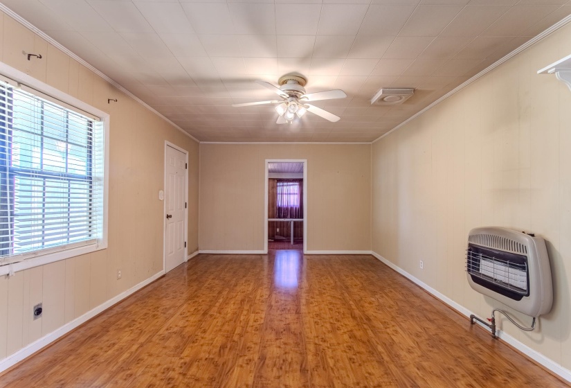 Unfurnished living room featuring wood finished floors, wood walls, heating unit, ceiling fan, and ornamental molding