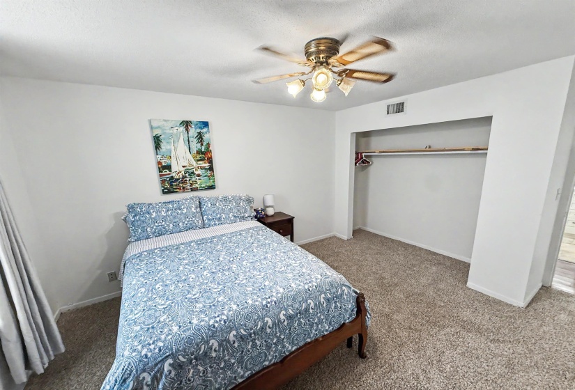 Bedroom featuring plush carpeting, a built-in closet with hanging rod and shelf, ceiling fan with light fixture, and white painted walls