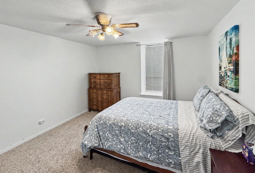 Carpeted bedroom featuring a ceiling fan with integrated lighting, a single window with blinds and drapery, and neutral wall tones