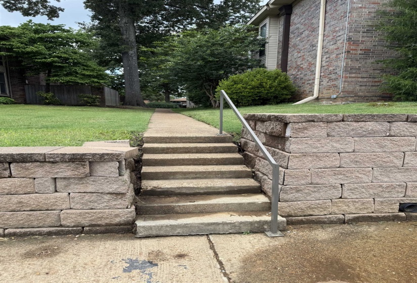 Concrete steps with a metal handrail, flanked by stone-block retaining walls