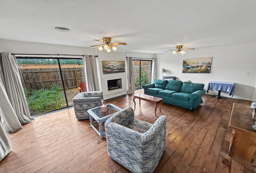 Spacious interior featuring wood-finish flooring, a white-painted brick fireplace, and sliding glass doors opening to outdoor space