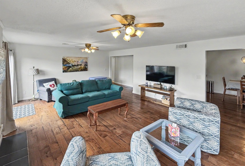 Spacious living area featuring wood-finish flooring, white walls, and multiple ceiling fans with light fixtures