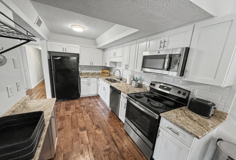 Kitchen featuring white cabinetry, wood-finish flooring, light-toned countertops, a white subway tile backsplash, and stainless steel appliances