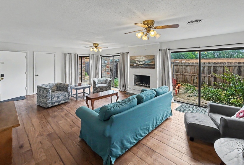 Living area featuring wood-finish flooring, a white-painted brick fireplace, and dual sliding glass doors leading to an outdoor space