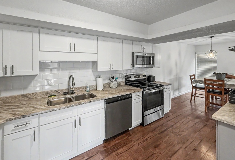 Kitchen featuring white cabinetry, subway tile backsplash, stainless steel appliances, dual basin sink with gooseneck faucet, and wood-finish flooring