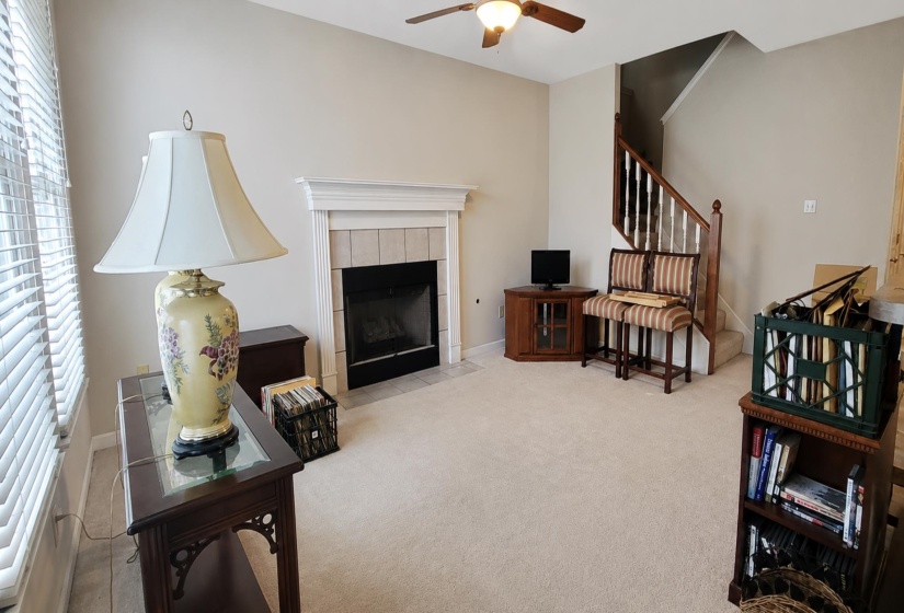 Living area with a fireplace featuring a white mantel and tile surround, light neutral carpeting, and a ceiling fan with integrated lighting
