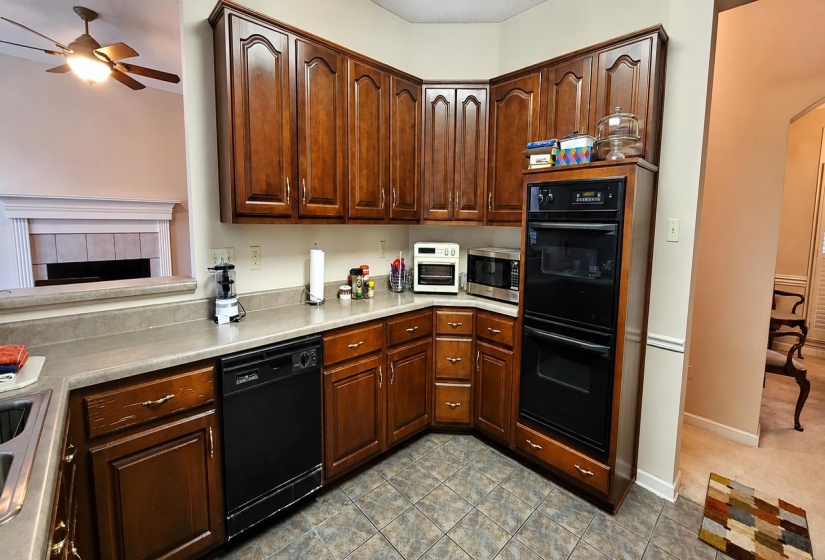 Kitchen featuring wood cabinetry, stone-finish countertops, tile flooring, built-in double ovens, and a built-in dishwasher