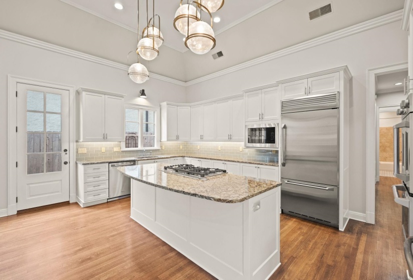 Gourmet kitchen featuring a large central island with gas cooktop, built in exhaust fan, granite countertops, stainless steel appliances, and an ideal layout for cooking and entertaining.