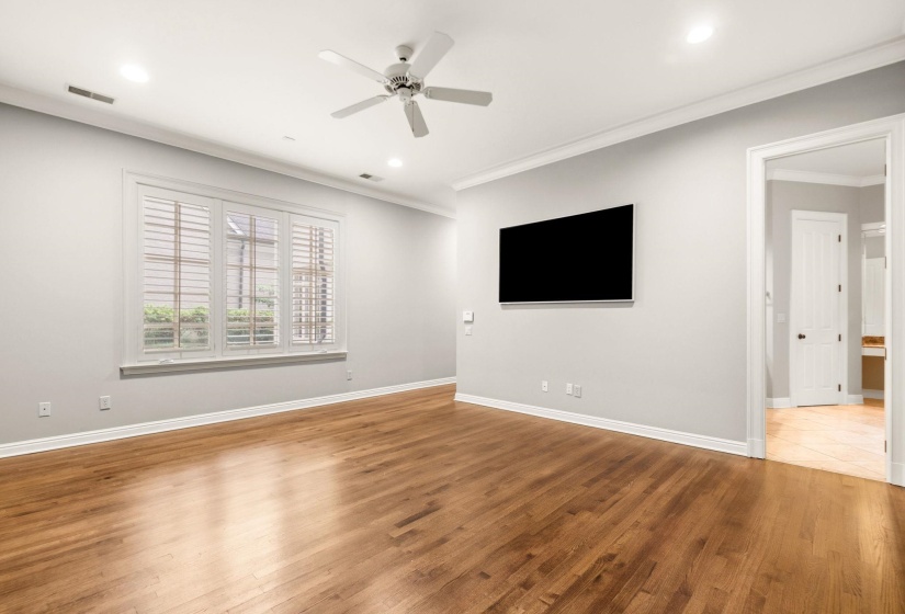 Serene primary suite featuring hardwood floors, recessed lighting, and a stunning wall of windows with peaceful backyard views, privately tucked away from the main living areas for ultimate comfort and tranquility.