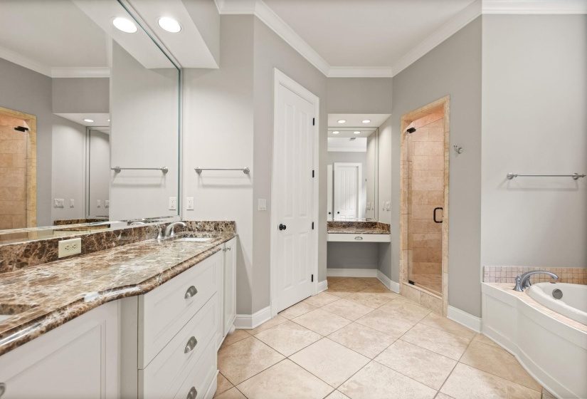 Spa-like primary bath featuring dual vanities, a built-in makeup vanity, glass-enclosed shower, expansive whirlpool soaking tub, tile flooring, and access to a massive walk-in closet.