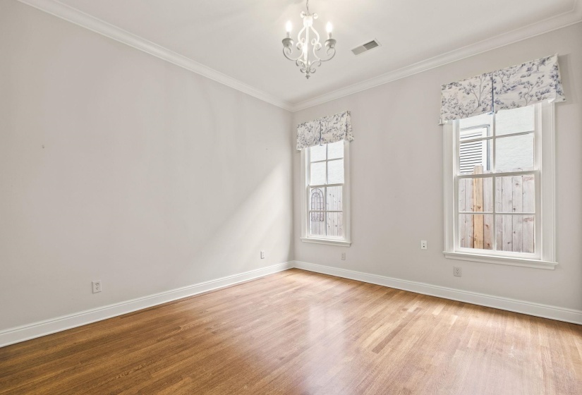 Versatile downstairs bedroom featuring hardwood floors, crown molding, and light neutral tones, with easy access to the kitchen and main living areas—perfect as a bedroom or home office.
