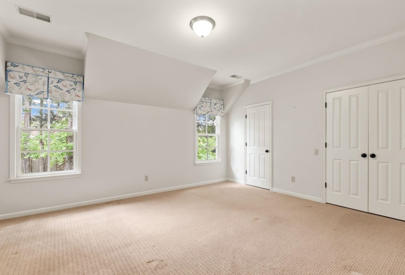 Inviting secondary suite upstairs featuring soft carpeting, abundant natural light from multiple windows, crown molding, charming architectural details, and a private en suite bathroom.