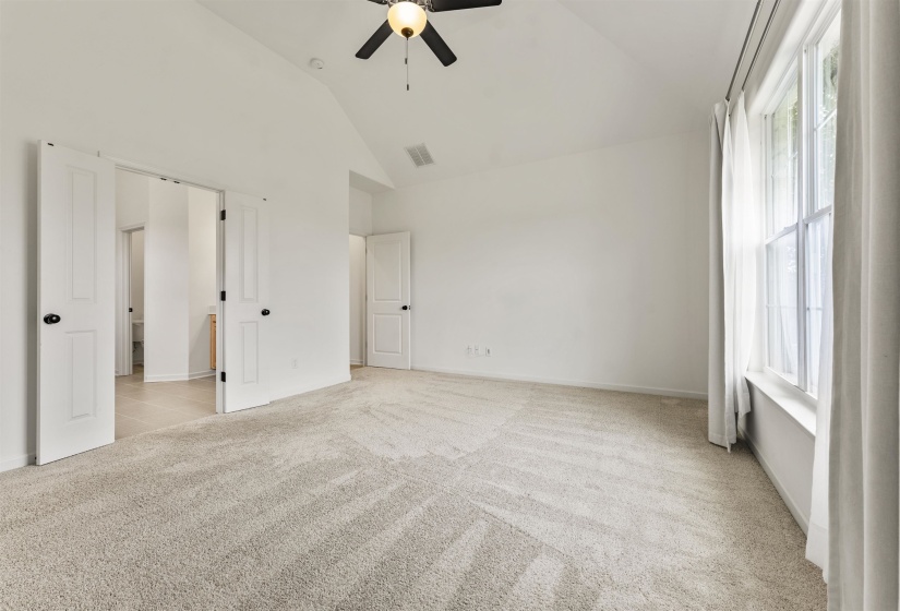 Spacious room featuring vaulted ceilings, a ceiling fan with integrated lighting, and light-toned carpet flooring