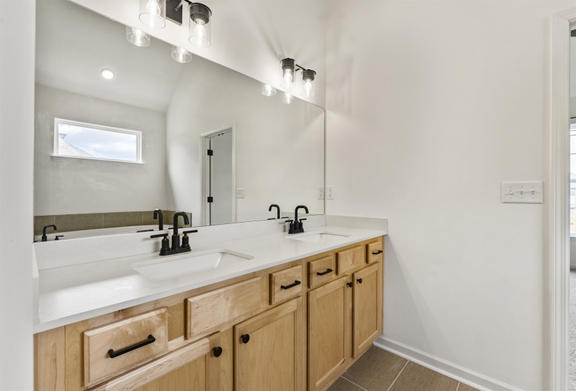 Dual vanity with light wood cabinetry, white countertops, and matte black fixtures