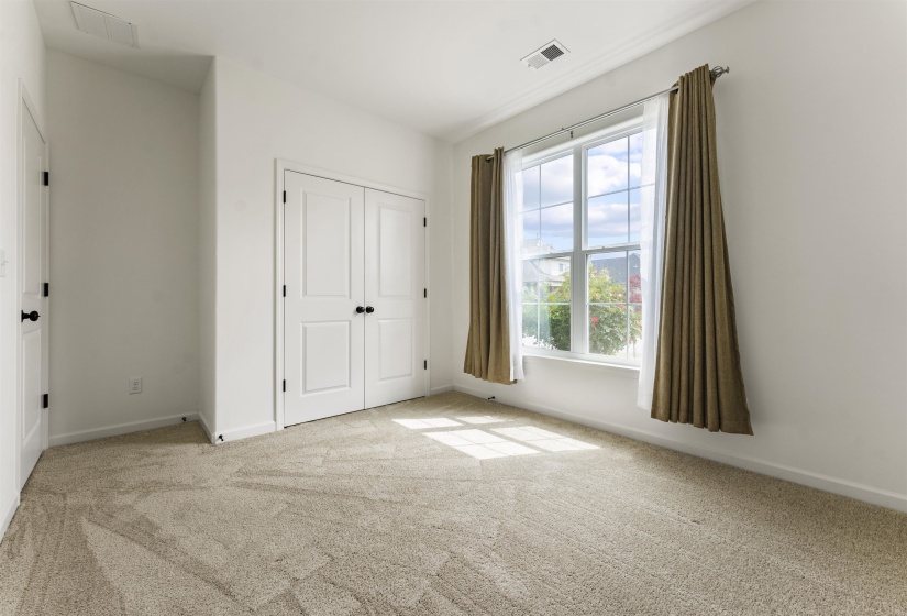 White-painted interior room featuring a double-pane window, neutral-toned carpeting, and white bi-fold doors with black hardware